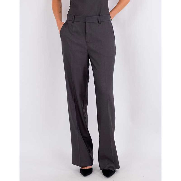 En kvinde står i en mørkegrå Neo Noir jumpsuit lavet af finkvalitet.